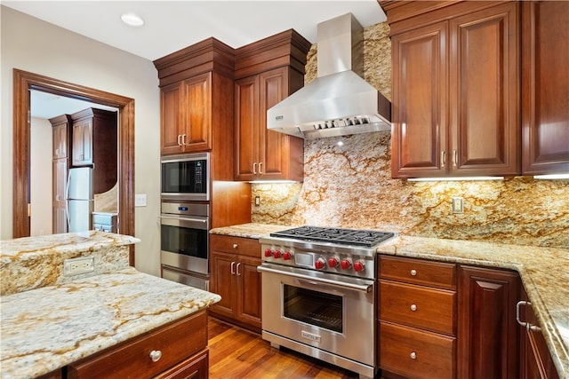 kitchen with stainless steel appliances, wall chimney exhaust hood, light hardwood / wood-style floors, and light stone counters