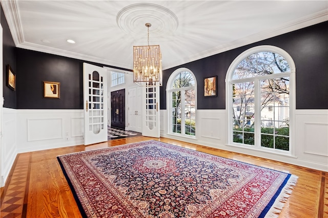 foyer with an inviting chandelier, wood-type flooring, ornamental molding, and plenty of natural light