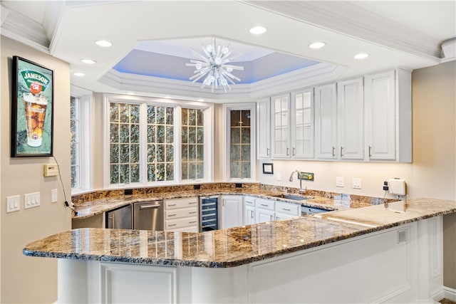 kitchen with stone counters, sink, white cabinets, beverage cooler, and a tray ceiling