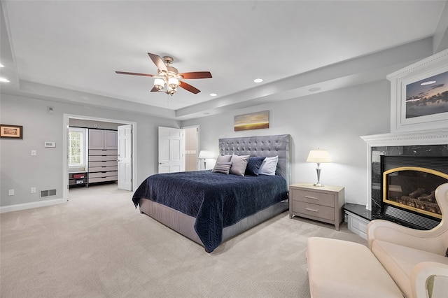 carpeted bedroom featuring ceiling fan, a raised ceiling, and a high end fireplace