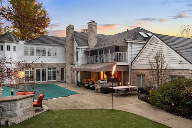 back house at dusk featuring outdoor lounge area, a patio, a balcony, and a covered pool