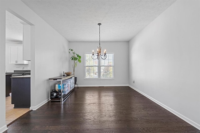 unfurnished dining area featuring wood-type flooring, a textured ceiling, and an inviting chandelier