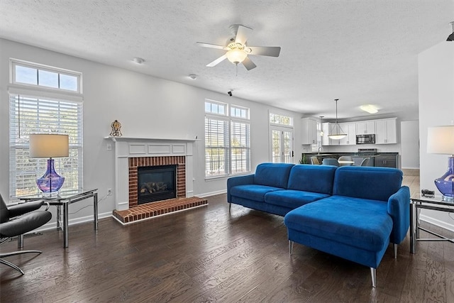 living room with dark hardwood / wood-style flooring, a textured ceiling, a healthy amount of sunlight, and a brick fireplace