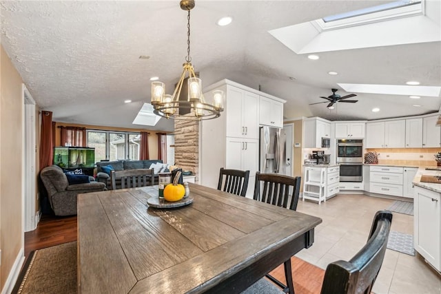 dining area featuring lofted ceiling with skylight, ceiling fan with notable chandelier, light tile patterned floors, and a textured ceiling