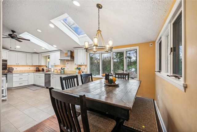 tiled dining space with lofted ceiling with skylight, sink, ceiling fan with notable chandelier, and a textured ceiling