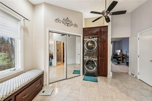 laundry area with a textured ceiling, ceiling fan, and stacked washing maching and dryer