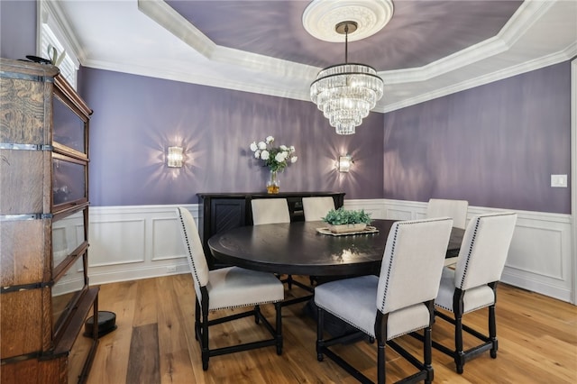 dining space featuring a raised ceiling, a notable chandelier, ornamental molding, and light hardwood / wood-style flooring