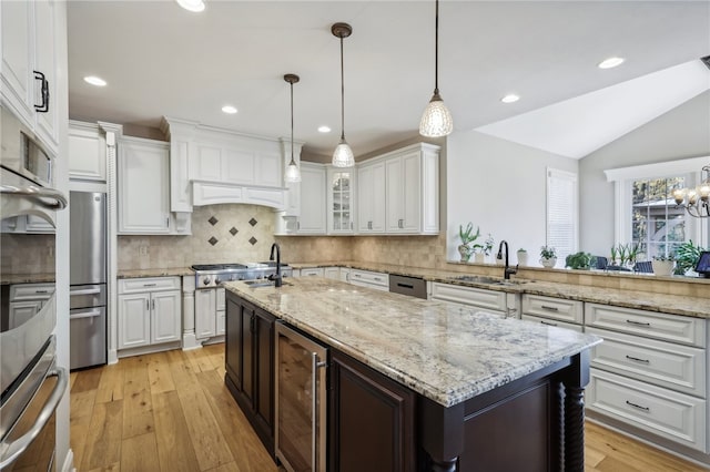 kitchen featuring beverage cooler, sink, an island with sink, pendant lighting, and light wood-type flooring