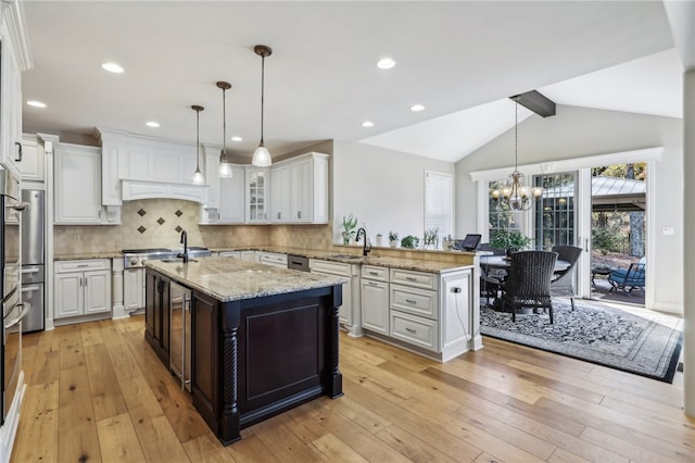 kitchen with a center island with sink, light hardwood / wood-style flooring, vaulted ceiling, and decorative light fixtures