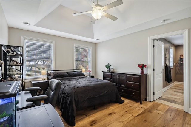 bedroom with a raised ceiling, ceiling fan, and light hardwood / wood-style flooring