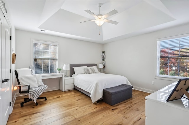 bedroom with ceiling fan, a raised ceiling, and light hardwood / wood-style flooring