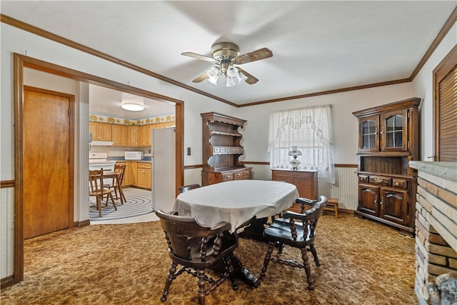 dining area featuring wood walls, light carpet, ornamental molding, ceiling fan, and a fireplace