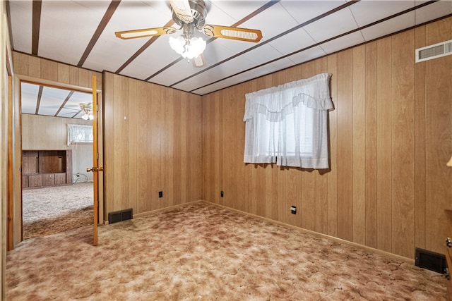 carpeted spare room featuring wood walls and ceiling fan