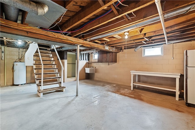 basement featuring water heater, white refrigerator, and sink