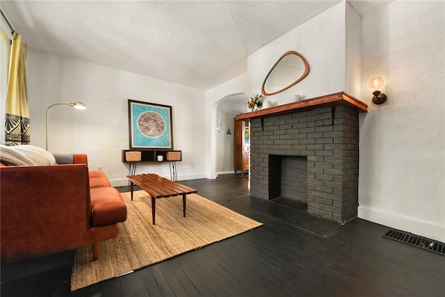 living room featuring a brick fireplace, dark hardwood / wood-style floors, and a textured ceiling