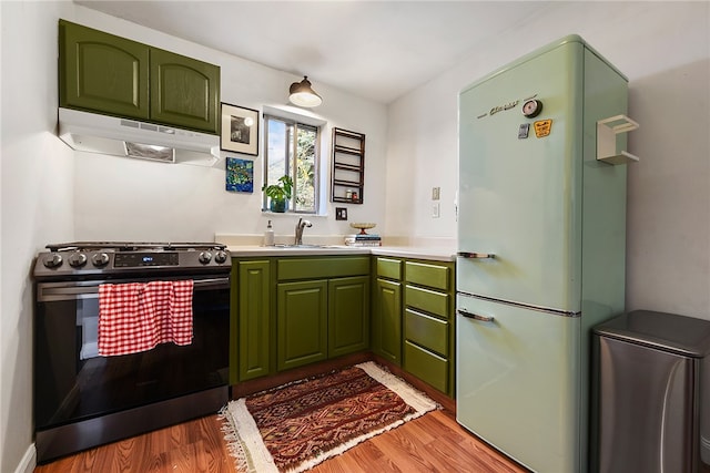 kitchen featuring stainless steel range with electric cooktop, white fridge, light wood-type flooring, green cabinetry, and sink