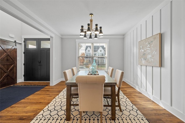 dining area with a chandelier, a barn door, ornamental molding, and wood-type flooring