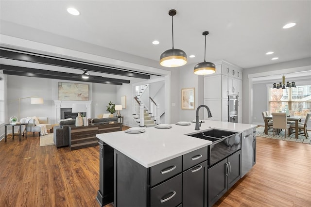 kitchen with sink, decorative light fixtures, an island with sink, stainless steel dishwasher, and dark wood-type flooring