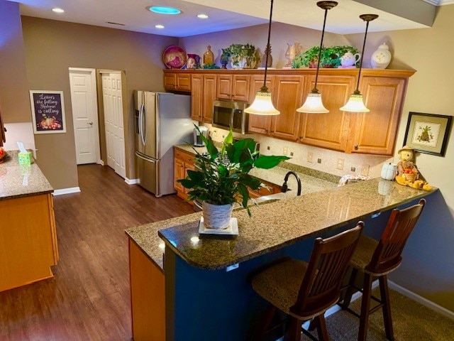 kitchen featuring appliances with stainless steel finishes, dark hardwood / wood-style floors, pendant lighting, a kitchen breakfast bar, and kitchen peninsula