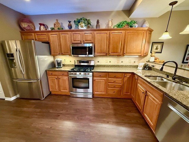 kitchen featuring stainless steel appliances, sink, light stone countertops, dark hardwood / wood-style floors, and pendant lighting