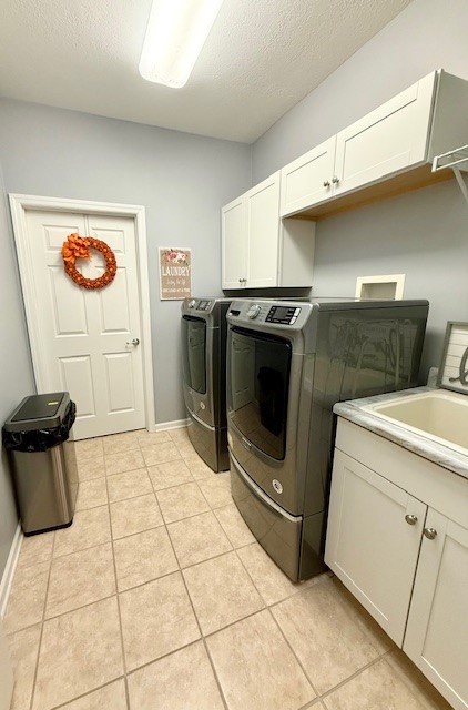 laundry room featuring cabinets, a textured ceiling, light tile patterned floors, and separate washer and dryer