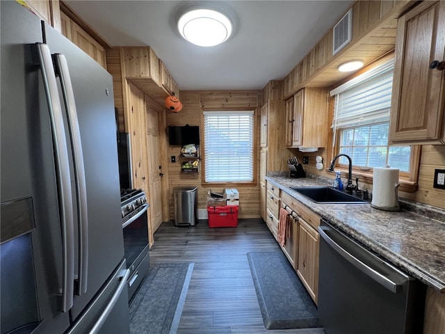 kitchen with wooden walls, sink, dark hardwood / wood-style floors, appliances with stainless steel finishes, and light brown cabinetry