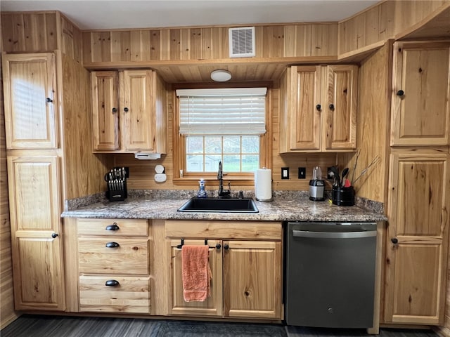 kitchen featuring light brown cabinets, wood walls, stainless steel dishwasher, and sink