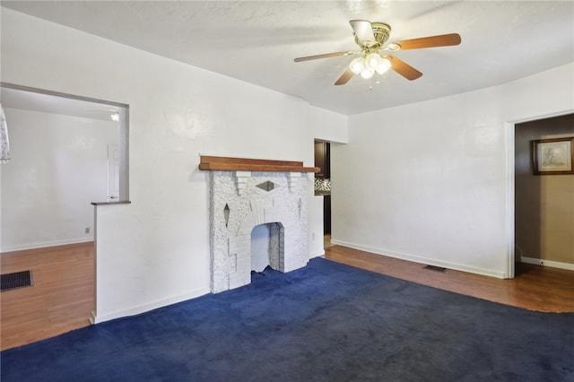 unfurnished living room with a brick fireplace, dark wood-type flooring, and ceiling fan