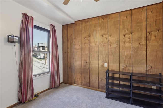 carpeted spare room with a wealth of natural light, ceiling fan, and wooden walls