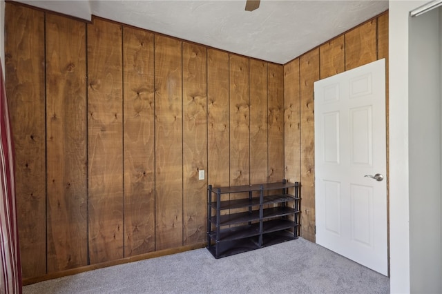 interior space featuring wood walls, light colored carpet, and ceiling fan