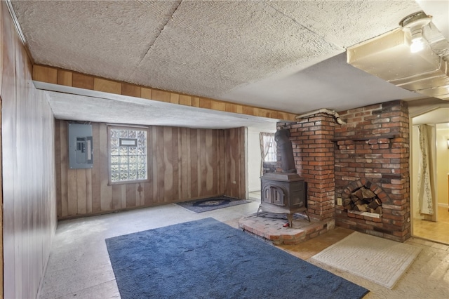 basement featuring electric panel, plenty of natural light, wooden walls, and a wood stove