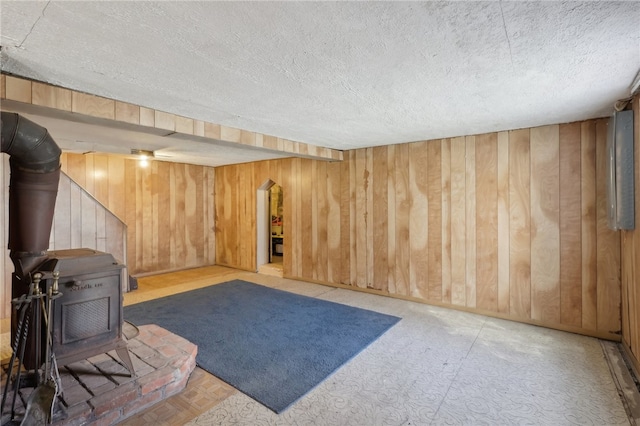 interior space with a wood stove, wood walls, and a textured ceiling