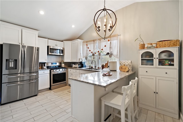 kitchen featuring white cabinetry, kitchen peninsula, stainless steel appliances, and vaulted ceiling