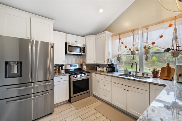 kitchen with white cabinets, stainless steel appliances, vaulted ceiling, and light stone countertops