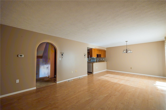 unfurnished living room with light hardwood / wood-style floors, a textured ceiling, and a notable chandelier