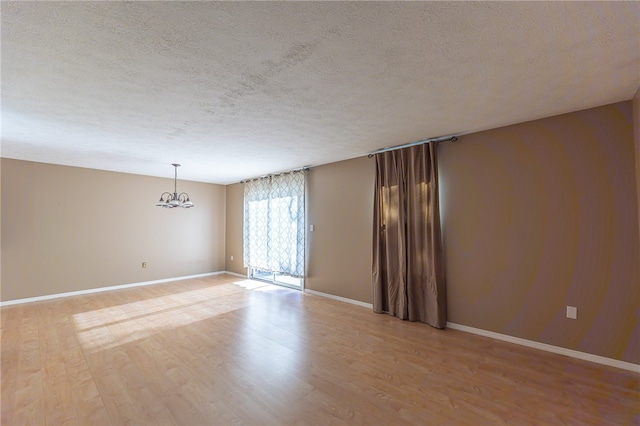 empty room with a chandelier, a textured ceiling, and light hardwood / wood-style flooring