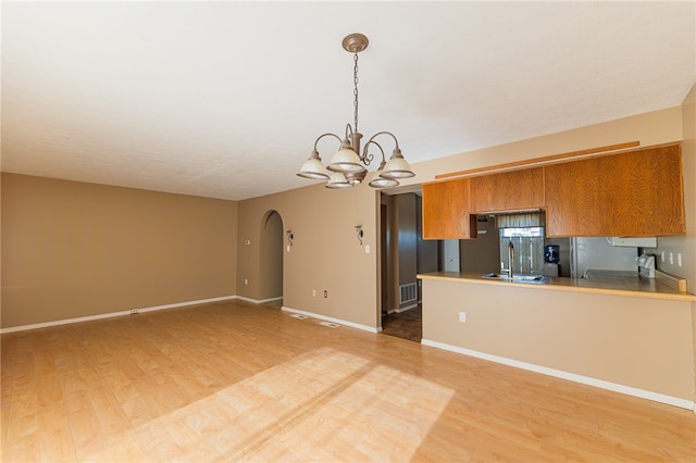 kitchen featuring wood-type flooring, kitchen peninsula, a notable chandelier, sink, and decorative light fixtures