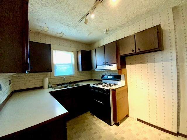 kitchen featuring a textured ceiling, rail lighting, sink, and gas range gas stove