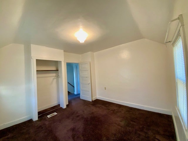 unfurnished bedroom featuring a closet, vaulted ceiling, and dark carpet