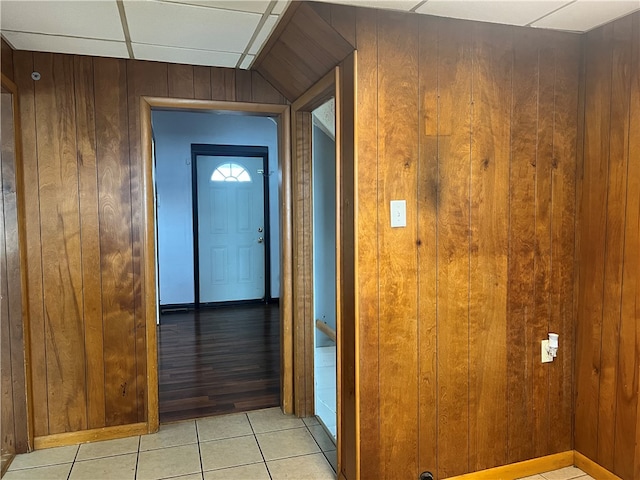 hallway featuring a drop ceiling, light wood-type flooring, and wooden walls