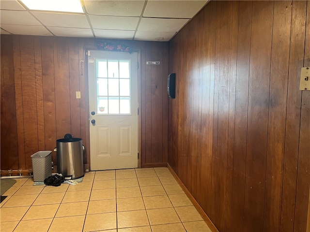 doorway to outside featuring wood walls, a drop ceiling, and light tile patterned flooring