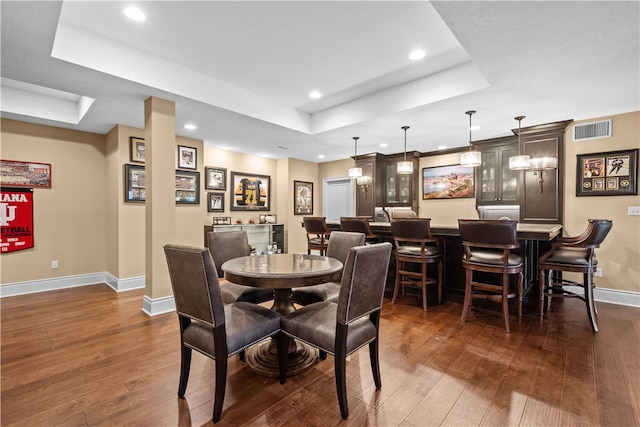 dining room with dark wood-type flooring, bar area, and a raised ceiling