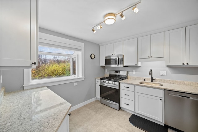 kitchen featuring stainless steel appliances, sink, track lighting, light stone counters, and white cabinets