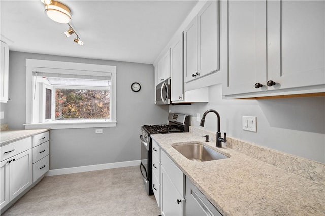 kitchen with white cabinetry, stainless steel appliances, sink, and light stone counters