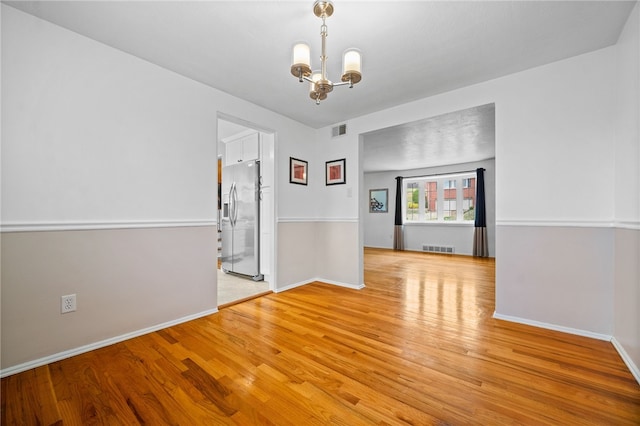 unfurnished room with light hardwood / wood-style flooring and a notable chandelier