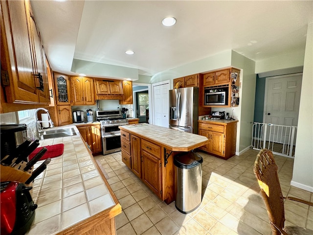 kitchen with tile countertops, sink, light tile patterned floors, a kitchen island, and appliances with stainless steel finishes