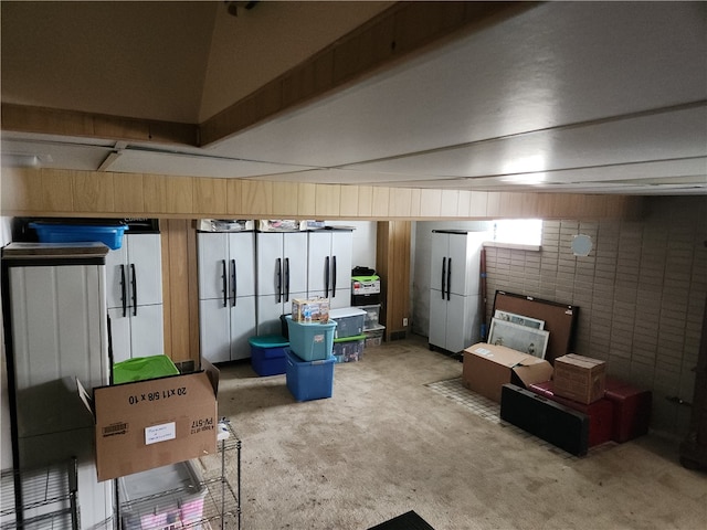 basement featuring carpet flooring, brick wall, and white refrigerator