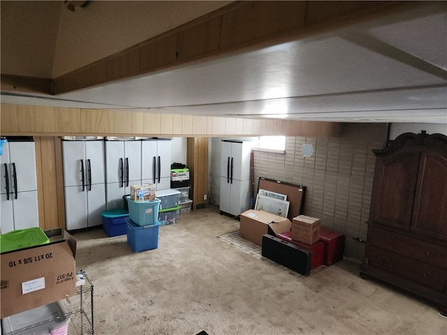 basement featuring light carpet, white fridge, and brick wall