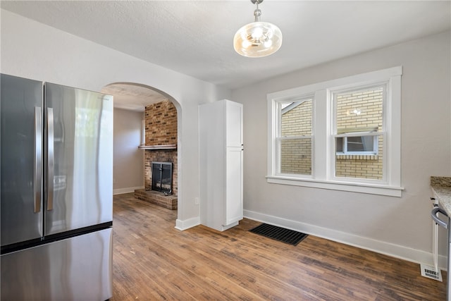 kitchen featuring a brick fireplace, light stone counters, hardwood / wood-style floors, white cabinetry, and stainless steel refrigerator