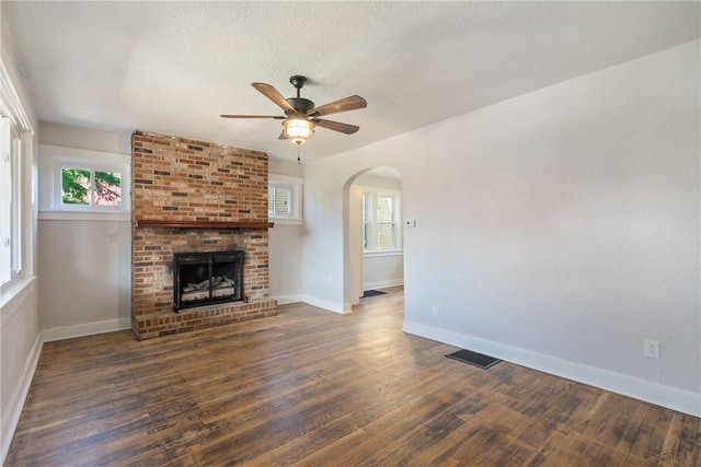 unfurnished living room with ceiling fan, dark hardwood / wood-style flooring, a healthy amount of sunlight, and a brick fireplace